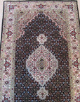 Ophelia Amara Brown Hand Knotted Wool Rug, showcasing intricate geometric patterns in warm brown tones, lies flat on a light wooden floor, its soft texture inviting touch in a bright, airy living space.