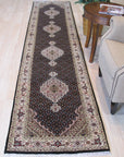 Ophelia Amara Brown Hand Knotted Wool Rug, displaying intricate patterns in shades of brown and cream, lays flat on a light wooden floor, its hand-knotted texture subtly visible.