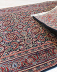 Sleek Oriental Navy Hand Knotted Wool Rug displayed in a warmly lit living space. Navy and cream hues interplay across the rug's traditional oriental pattern. Soft wool fibers and intricate knotting are visible in the design.