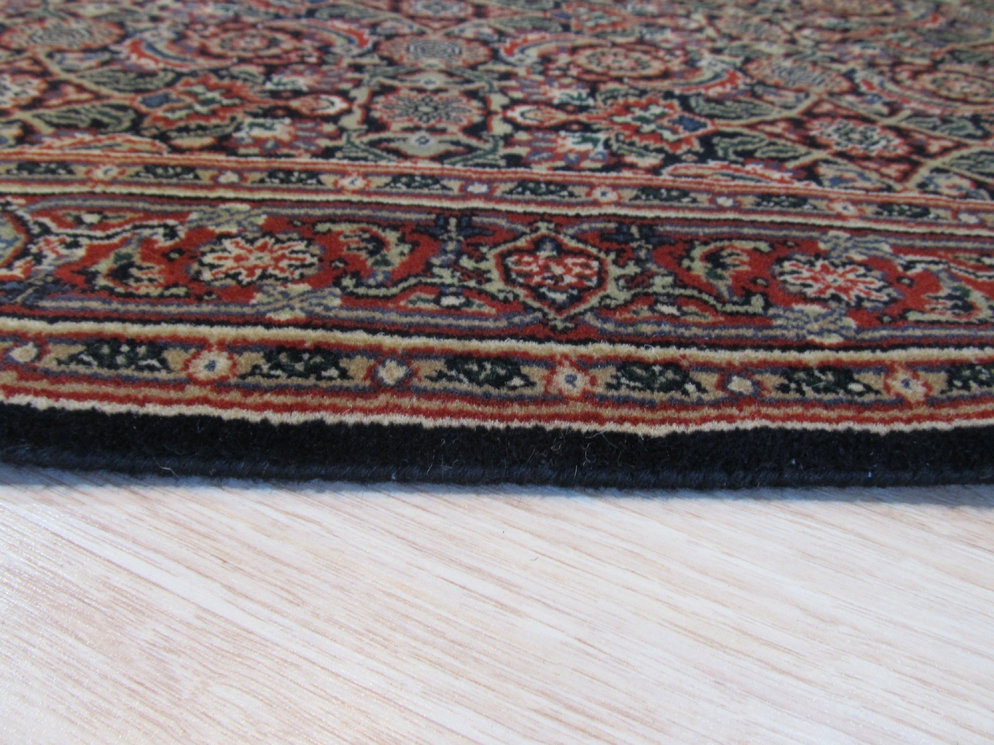 Sleek Oriental Navy Hand Knotted Wool Rug, its deep navy field detailed with traditional patterns in lighter hues, lies anchored in a warmly lit room; hardwood floors and neutral walls create a sophisticated backdrop for the luxurious wool texture.