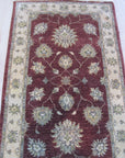 Timeless Oushak Red Hand Knotted Wool Rug, its intricate floral and geometric patterns rendered in rich reds and creams, lies gracefully on a light hardwood floor, suggesting warmth and elegance within a living space.