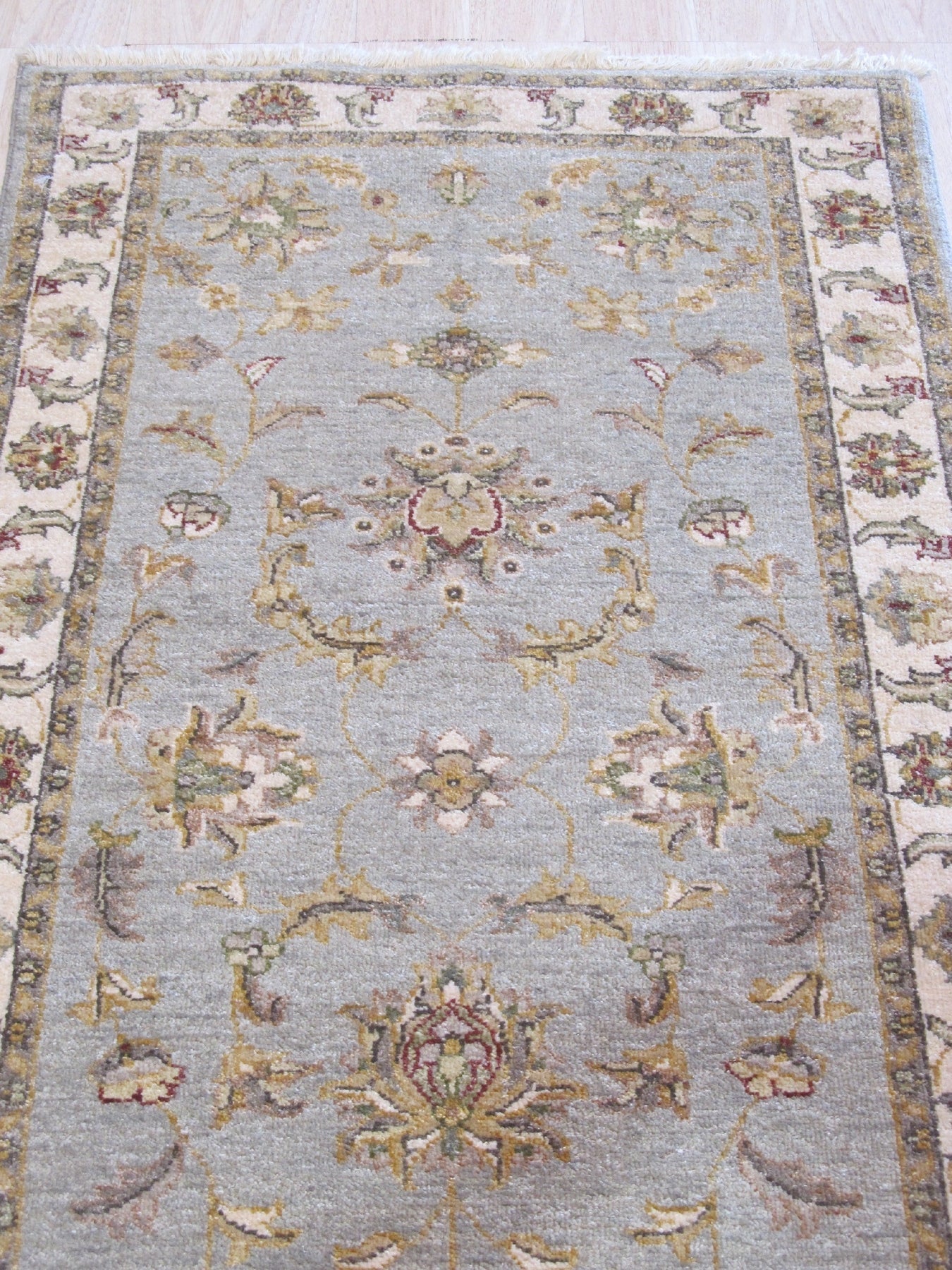 Zinnia Agra Green Hand Knotted Wool Rug displayed on a light hardwood floor, its intricate floral pattern in shades of green and cream adding a touch of traditional elegance to the room.