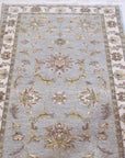 Zinnia Agra Green Hand Knotted Wool Rug displayed on a light hardwood floor, its intricate floral pattern in shades of green and cream adding a touch of traditional elegance to the room.
