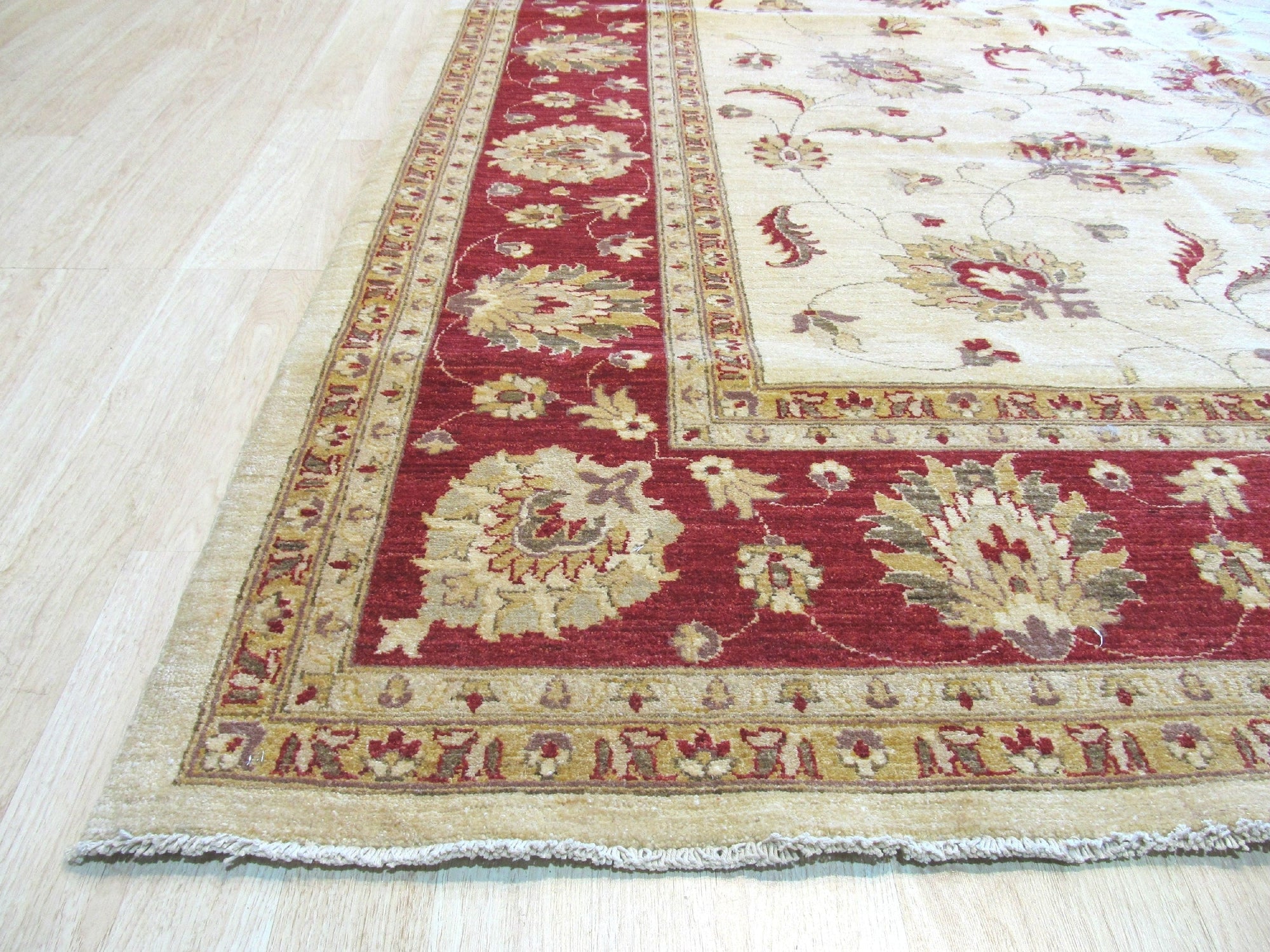 Trara Peshawar Multicolor Hand Knotted Wool Rug, showcasing vibrant geometric patterns woven in shades of crimson, gold, indigo, and olive, lies on a light hardwood floor, its textured surface reflecting subtle natural light.