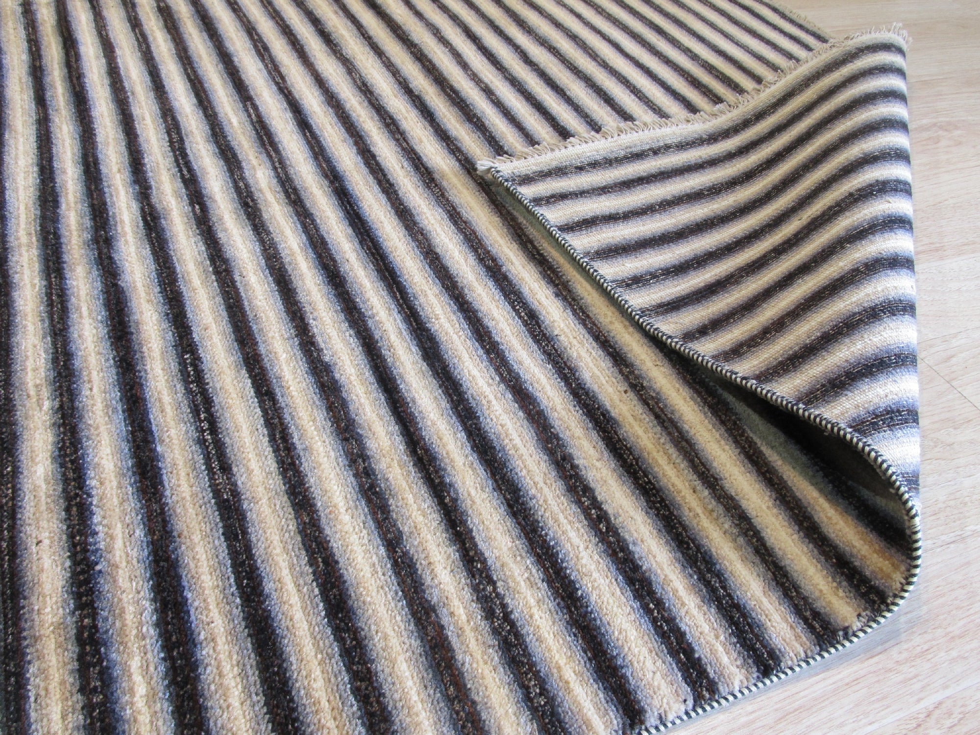 Isla Striped Multicolor Hand Knotted Wool Rug displayed in a bright, naturally lit living room setting. Warm and cool tones blend in a captivating striped pattern across the hand-knotted wool texture, grounded by light hardwood floors and complemented by a minimalist, modern aesthetic.