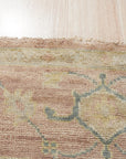 Timeless Oushak Pink Hand Knotted Wool Rug, displaying a delicate floral pattern in soft pink hues, graces a bright living space with warm wooden floors, hinting at classic elegance and handcrafted comfort.