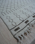 Jasmine Moroccan Ivory Hand Knotted Wool Rug, its plush ivory wool pile displaying a subtle geometric Moroccan pattern, rests serenely in a bright, airy living space.