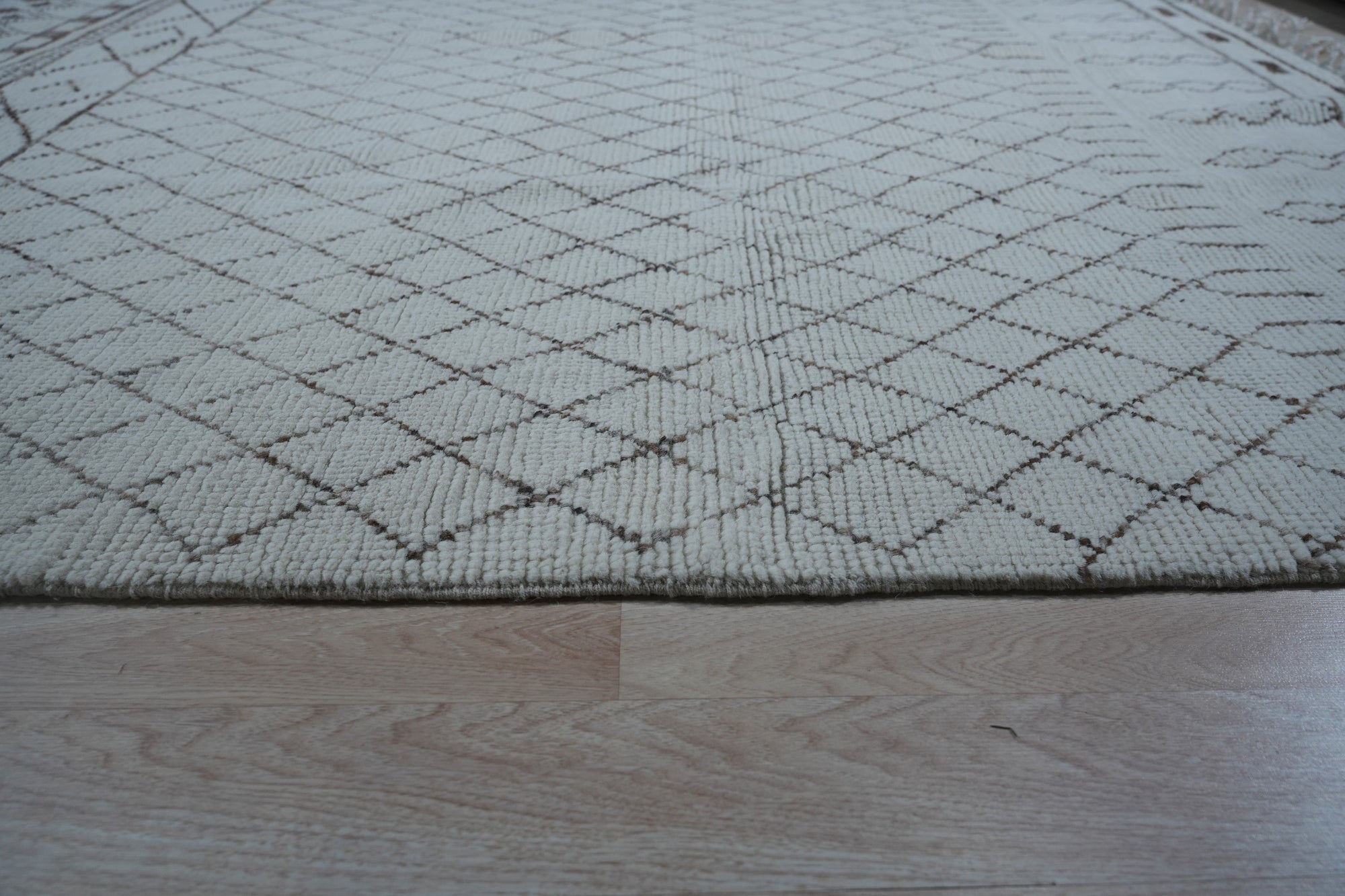 Jasmine Moroccan Ivory Hand Knotted Wool Rug in a bright, airy living space. Hand-knotted texture visible with geometric diamond patterns in ivory tones covering the wool pile. Modern furniture complements the rug's soft, bohemian aesthetic.