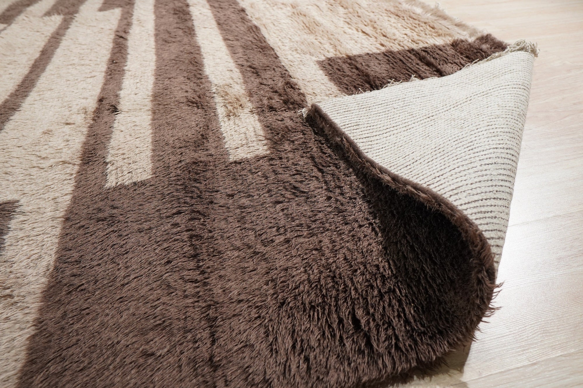 Nadia Mira Brown Hand Knotted Wool Rug, blending warm brown tones with intricate, geometric patterns, lies gracefully on a light wood floor, creating a cozy and inviting atmosphere.