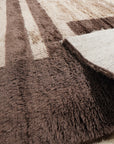 Nadia Mira Brown Hand Knotted Wool Rug, blending warm brown tones with intricate, geometric patterns, lies gracefully on a light wood floor, creating a cozy and inviting atmosphere.