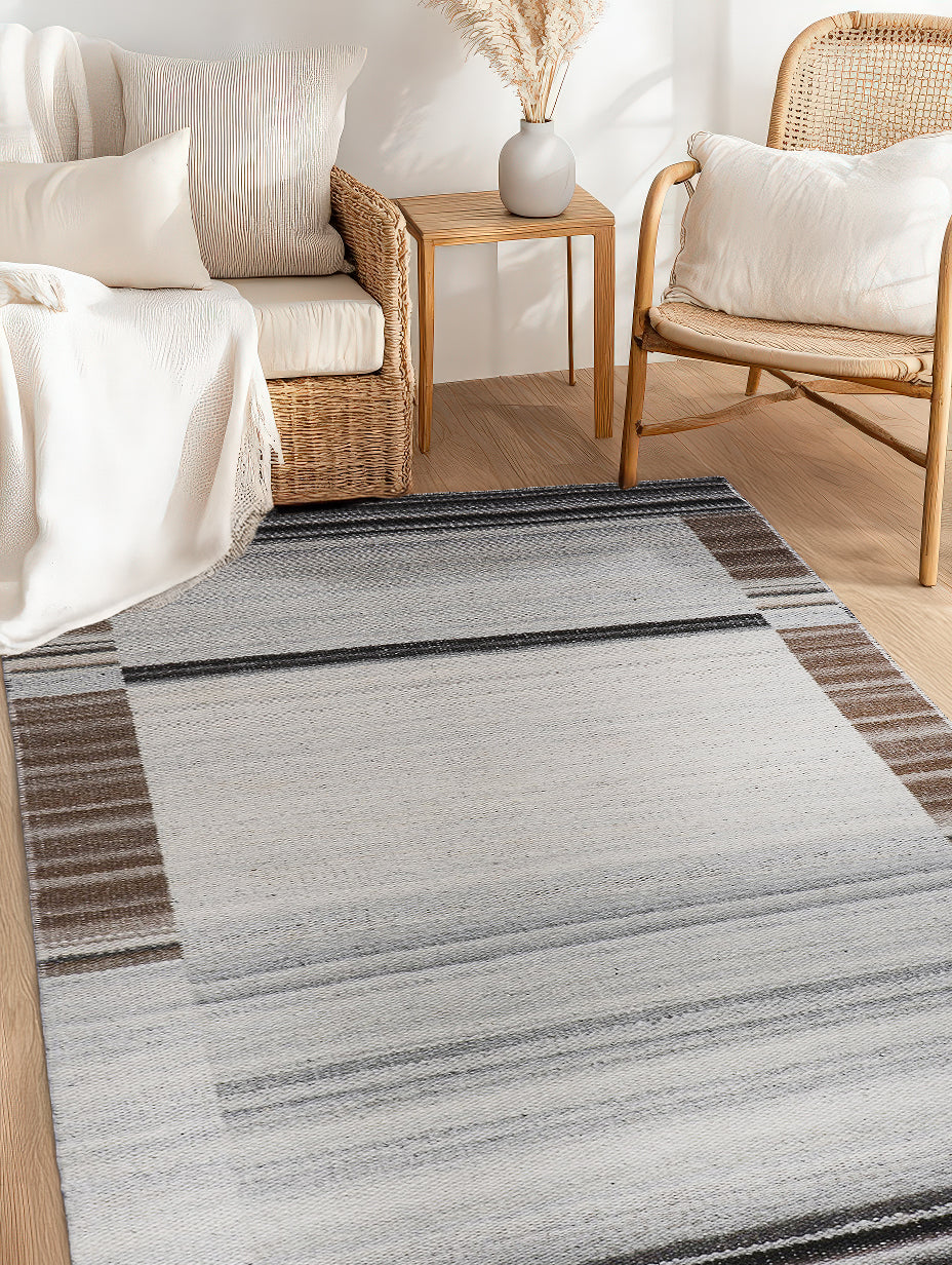 Classic Reversible Delicate Brown Flatweave Wool & Viscose Rug, seen in a warmly lit living room setting. Subtle pattern dances across its flatweave surface, blending seamlessly with the hardwood floor and neutral decor. The brown wool and viscose construction offers a sophisticated, textured feel.
