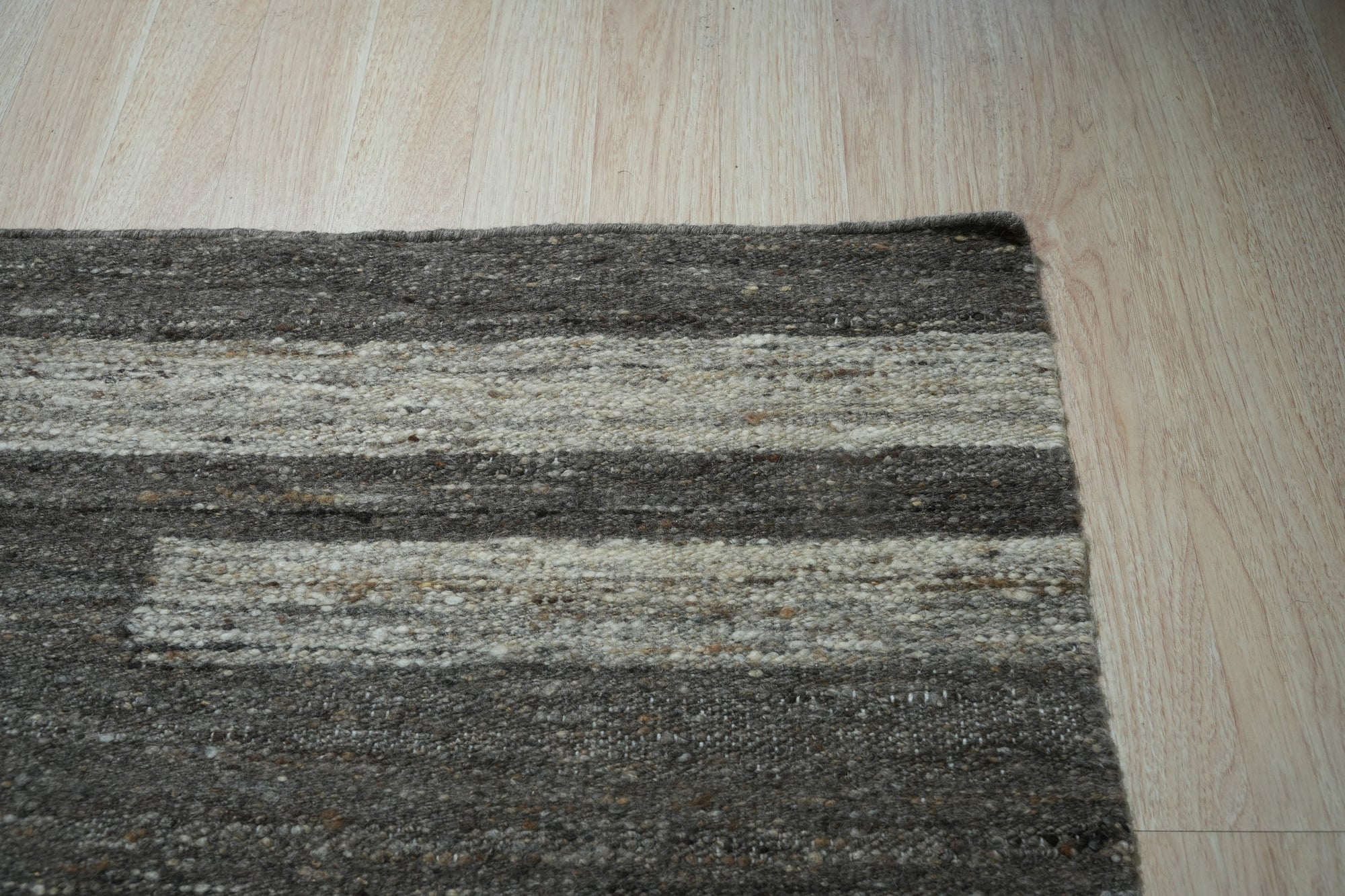 Cassandra Clara Brown Flatweave Wool Rug, a warm brown wool rug with a subtle geometric pattern, complementing a bright, minimalist living room with light wood flooring and a sleek black accent chair.