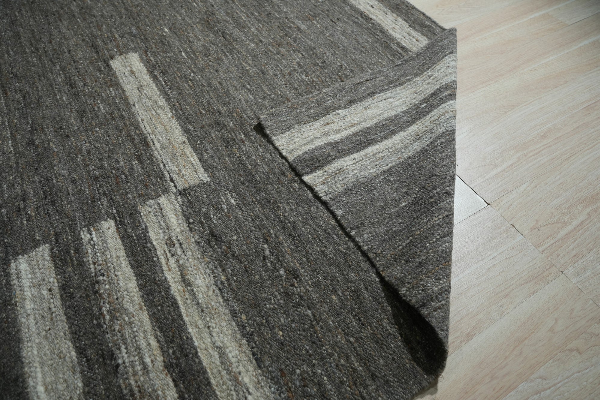 Cassandra Clara Brown Flatweave Wool Rug, showcasing subtle earth-toned patterns across its woven surface, situated in a sunlit room hinting at a warm, inviting atmosphere.