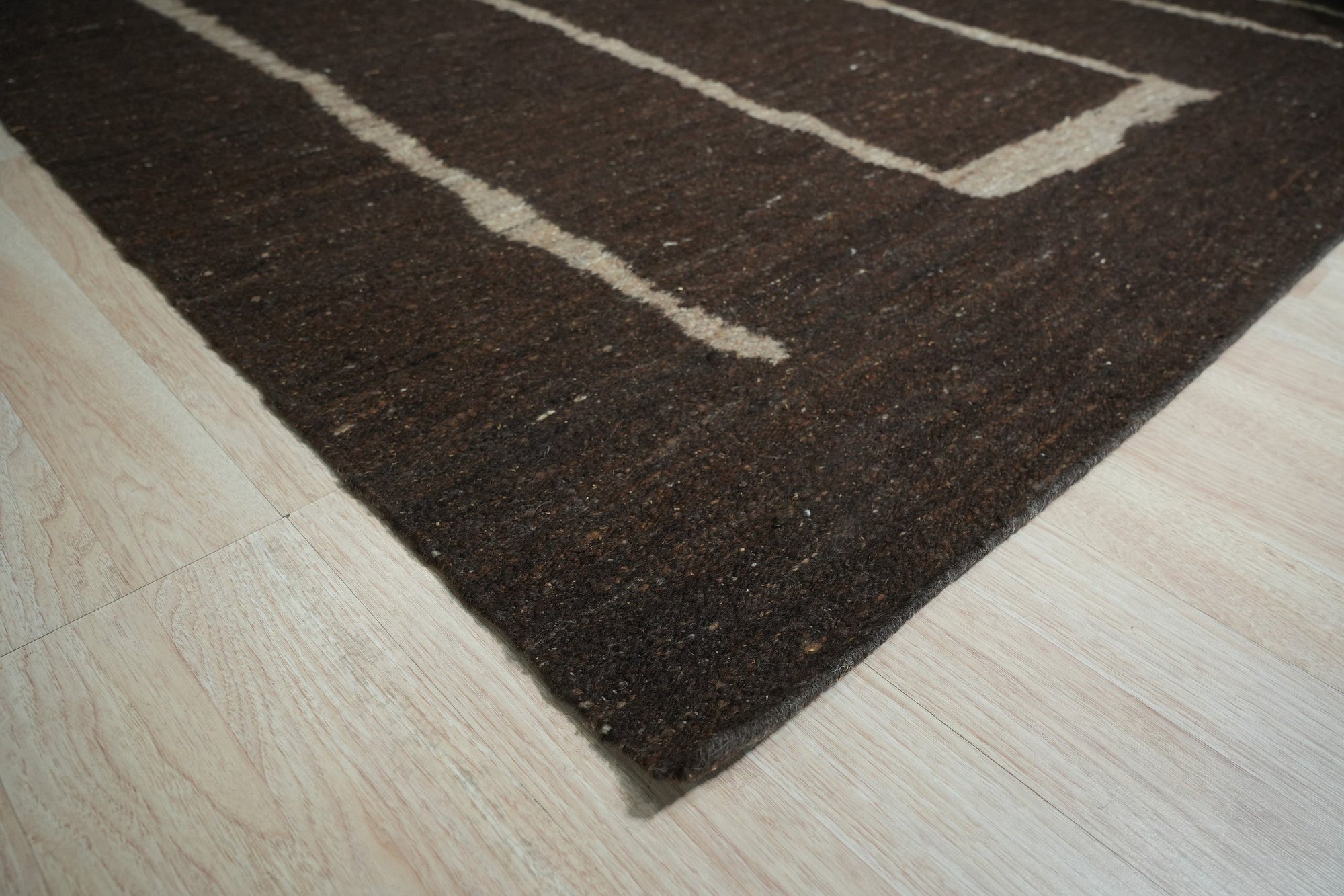 Talia Delicate Brown Flatweave Wool Rug, a brown flatweave wool rug with a subtle, textured pattern, seen in a bright living space, partially covered by a modern coffee table.