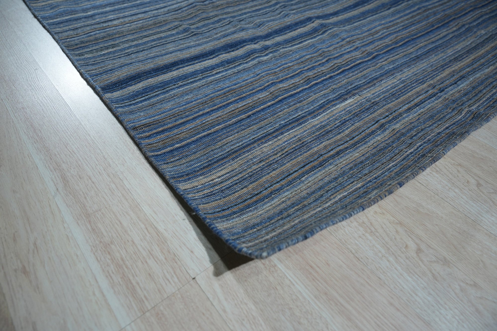 Freya Alluring Blue Handmade Rug, a blend of cerulean and indigo hues, lies gracefully on a polished wood floor, its intricate hand-knotted construction hinting at timeless elegance.