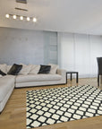 Maya Moroccan Black Flatweave Wool Rug, a striking geometric pattern in bold black against a light background, lies flat in a well-lit living space, adding a modern tribal touch to the room's decor.