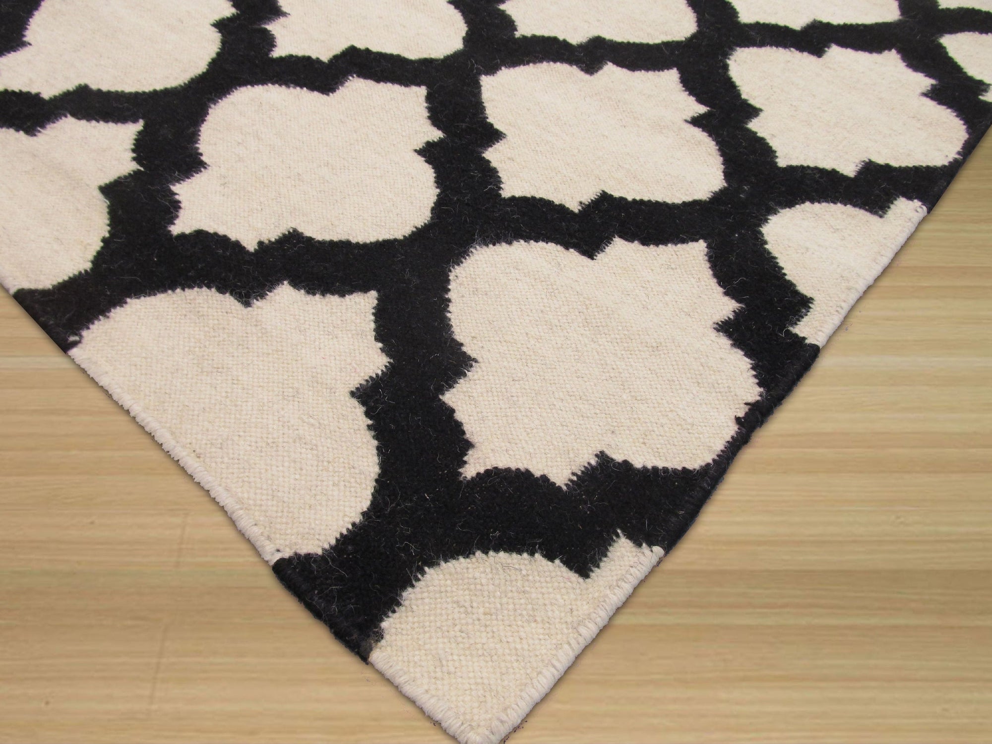 Maya Moroccan Black Flatweave Wool Rug, a black wool rug with a geometric Moroccan-inspired design, displayed in a bright, airy living room setting.