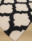 Maya Moroccan Black Flatweave Wool Rug, a black wool rug with a geometric Moroccan-inspired design, displayed in a bright, airy living room setting.