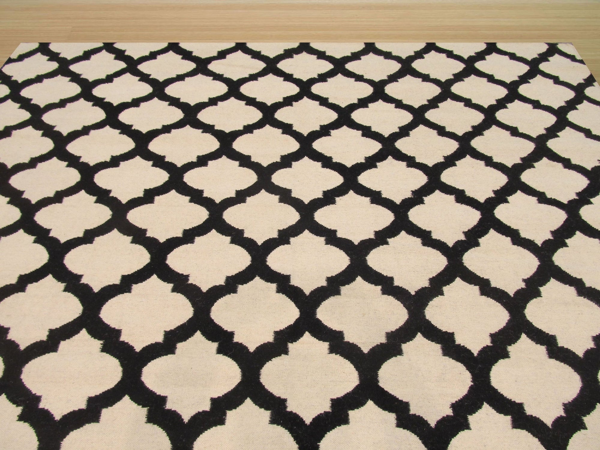 Maya Moroccan Black Flatweave Wool Rug, seen in a living room setting, its geometric black pattern contrasting against light wood floors and a neutral sofa.