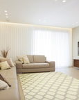 Maya Moroccan Ivory Flatweave Wool Rug graces a bright living room setting. Natural light illuminates its intricate geometric pattern woven in soft ivory wool. The rug anchors a seating area, offering a subtle yet elegant foundation for modern furnishings.