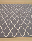 Classic Moroccan Gray Flatweave Wool Rug displayed in a living room setting. Soft gray wool forms a geometric pattern across the flatweave rug, contrasting subtly with the light hardwood floor. The rug anchors a seating area, lending a touch of understated Moroccan style.