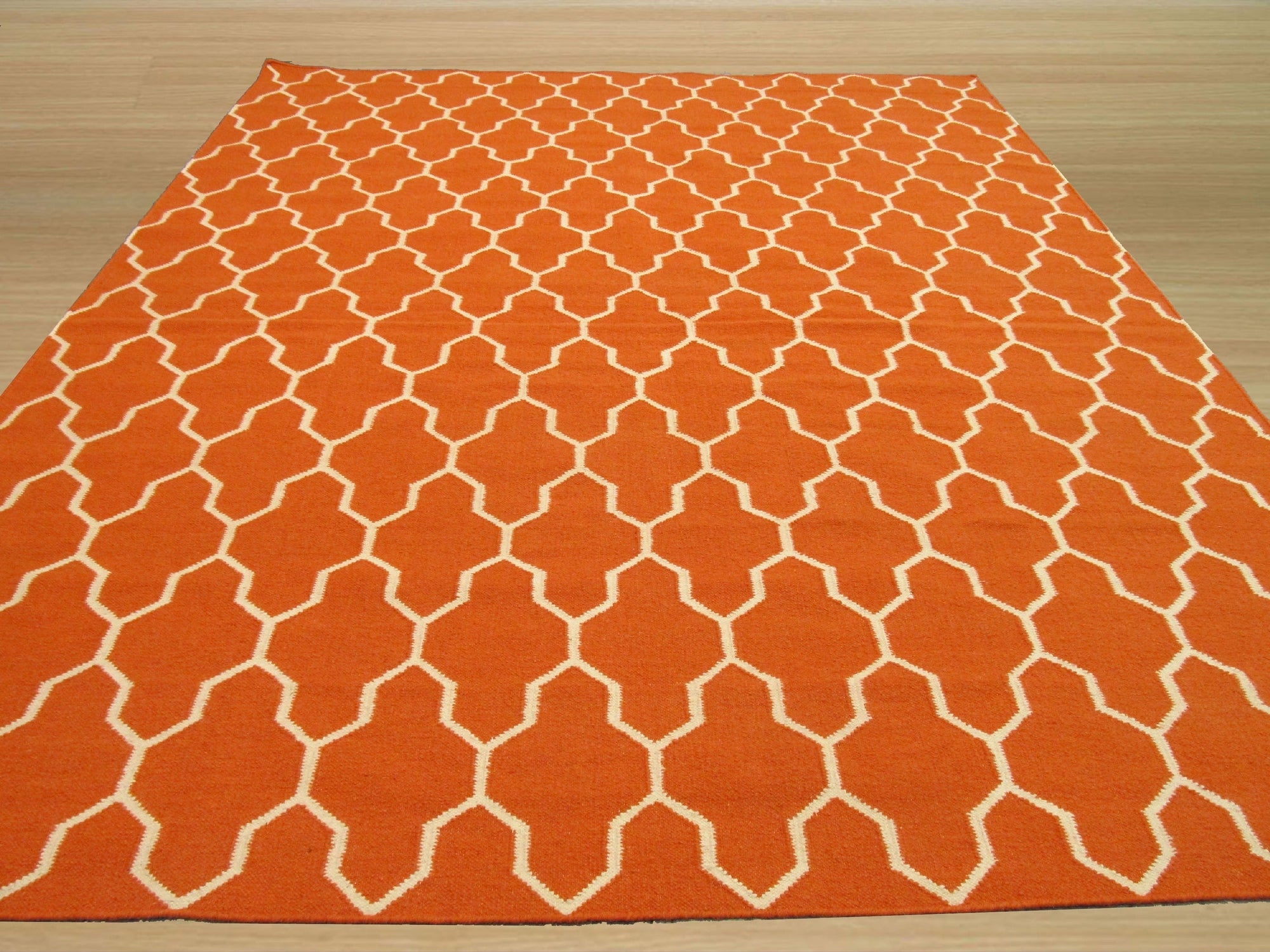 Classic Moroccan Orange Flatweave Wool Rug, showcasing its vibrant orange hues and traditional geometric patterns, lies flat on a light-colored wooden floor, creating a warm and inviting space.