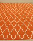 Classic Moroccan Orange Flatweave Wool Rug, showcasing its vibrant orange hues and traditional geometric patterns, lies flat on a light-colored wooden floor, creating a warm and inviting space.
