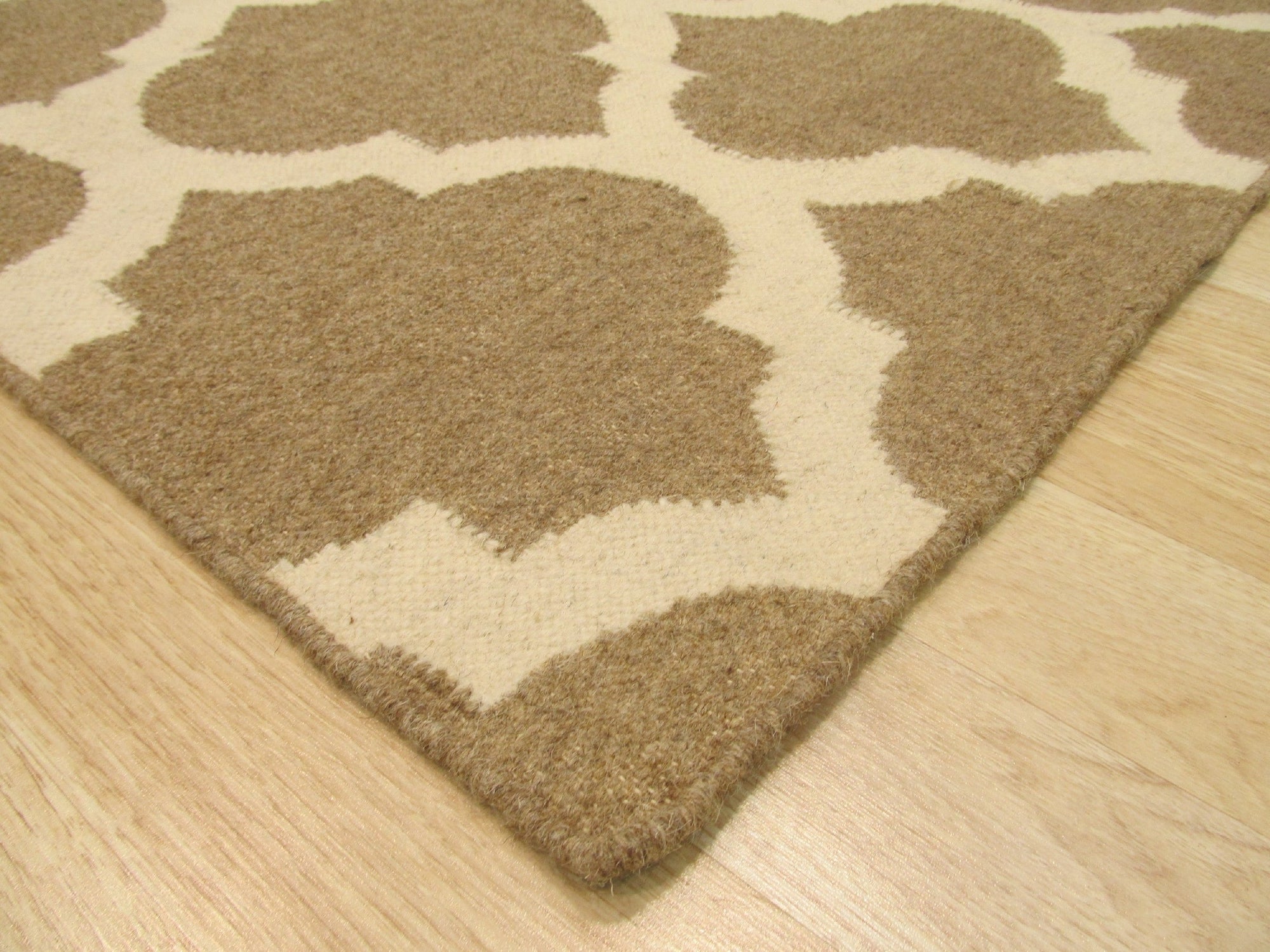 Iris Moroccan Brown Flatweave Wool Rug, showcasing its geometric Berber pattern in warm browns against a lighter background, lies flat on a hardwood floor, creating a welcoming, textured accent in a sunlit room.