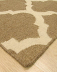 Iris Moroccan Brown Flatweave Wool Rug, showcasing its geometric Berber pattern in warm browns against a lighter background, lies flat on a hardwood floor, creating a welcoming, textured accent in a sunlit room.