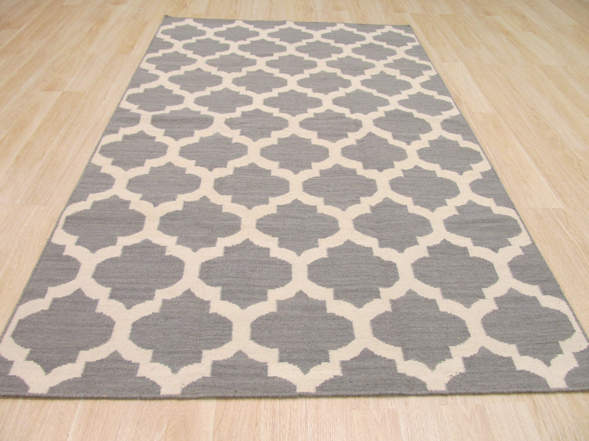 Selene Elena Gray Flatweave Wool Rug, showcasing a subtle geometric pattern in soft grays, lays flat in a brightly lit living space with contemporary furniture.
