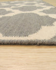 Selene Elena Gray Flatweave Wool Rug, subtly textured and light gray, anchoring a modern living space with a minimalist aesthetic, seen beneath a glass coffee table and complementing neutral furniture.