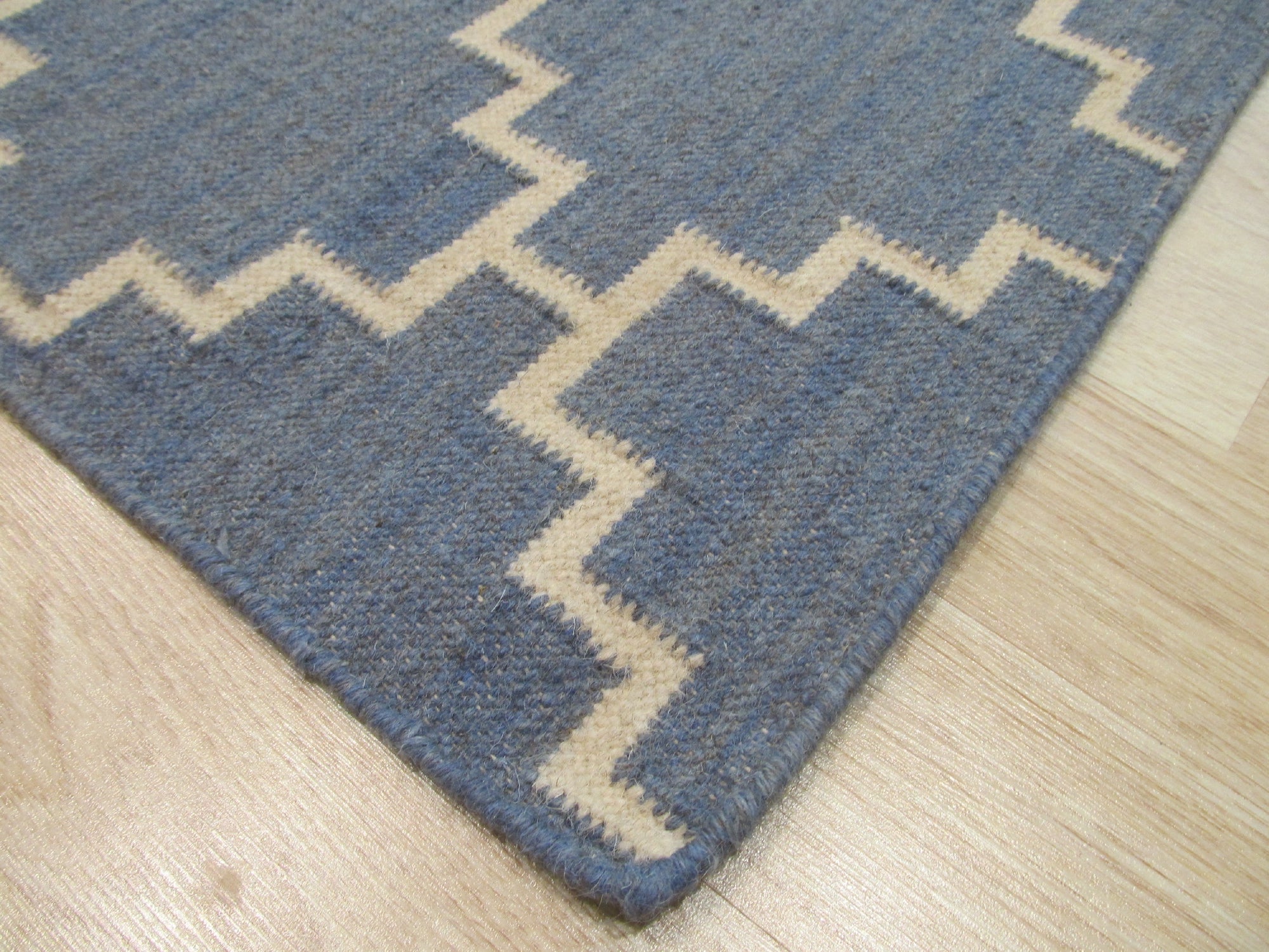 Alluring Bianca Blue Flatweave Wool Rug, a blend of cool blues and creamy whites creating a serene, subtly textured floor covering, displayed in a bright living room setting.
