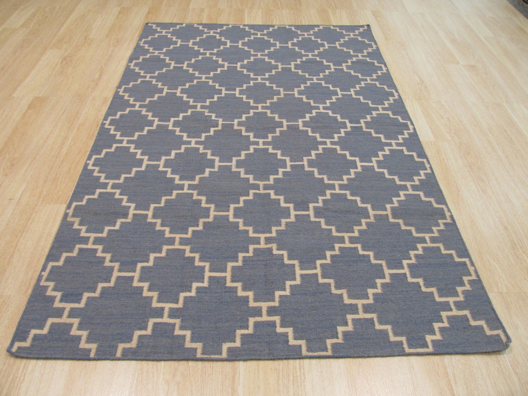Alluring Bianca Blue Flatweave Wool Rug, a calming blue flatweave wool rug with a subtle geometric pattern, lies grounded on a light hardwood floor, evoking a sense of serene sophistication in a naturally lit space.