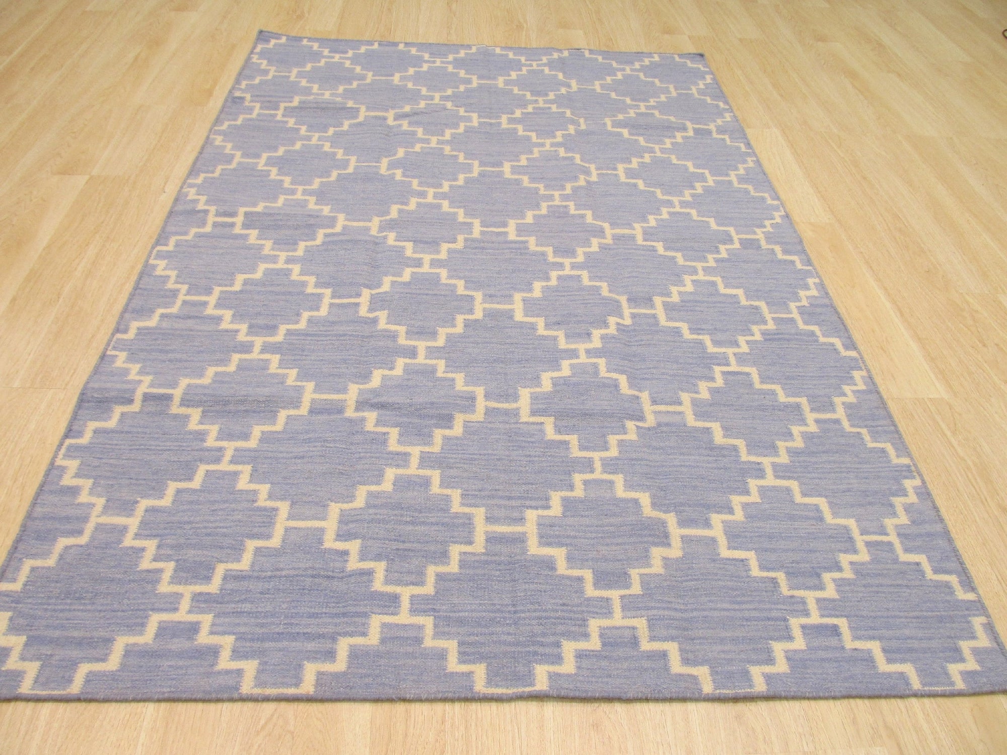 Ruby Moroccan Blue Flatweave Wool Rug, its cool blue tones and geometric Moroccan-inspired design complementing a modern living space with hardwood floors and a leather armchair.