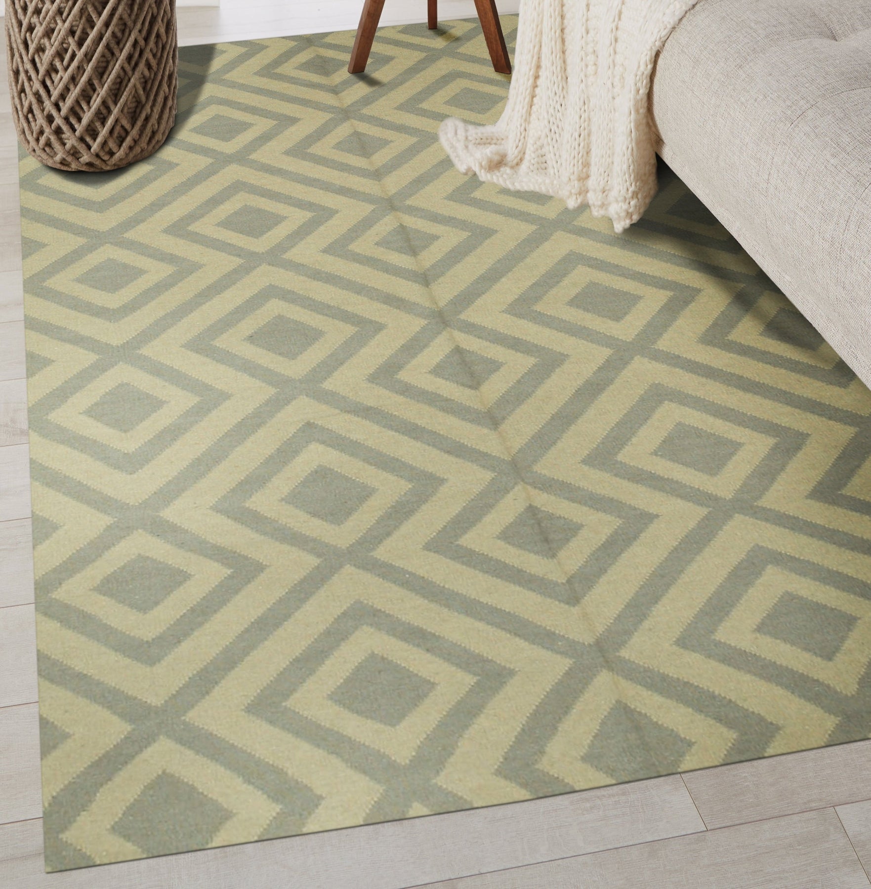 Quinn Kilim Beige Flatweave Wool Rug displayed in a bright living room setting. Warm, neutral tones and geometric patterns define this beige wool rug. A coffee table sits atop, anchoring the space and hinting at a comfortable, lived-in feel.