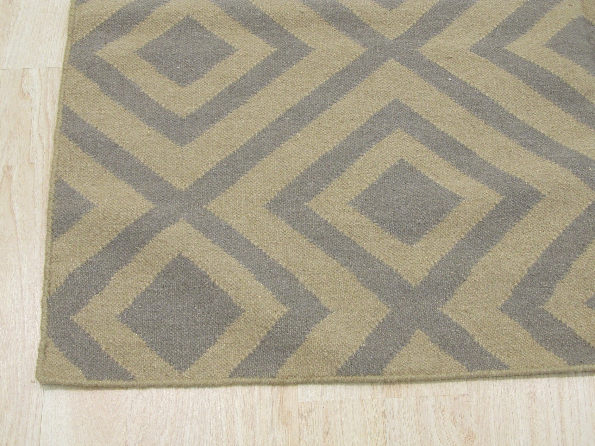 Quinn Kilim Beige Flatweave Wool Rug, featuring geometric patterns in neutral beige tones, layered atop a dark wood floor in a bright living space.