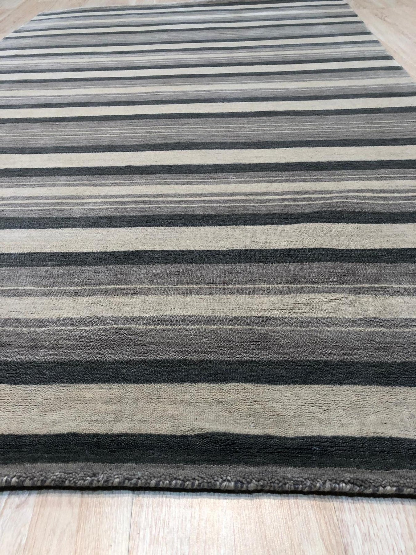 Serene Striped Multicolor Handmade Wool Rug, a handcrafted wool rug featuring vibrant stripes of varying widths in warm and cool tones, creating a textured and inviting floor covering within a contemporary living space.