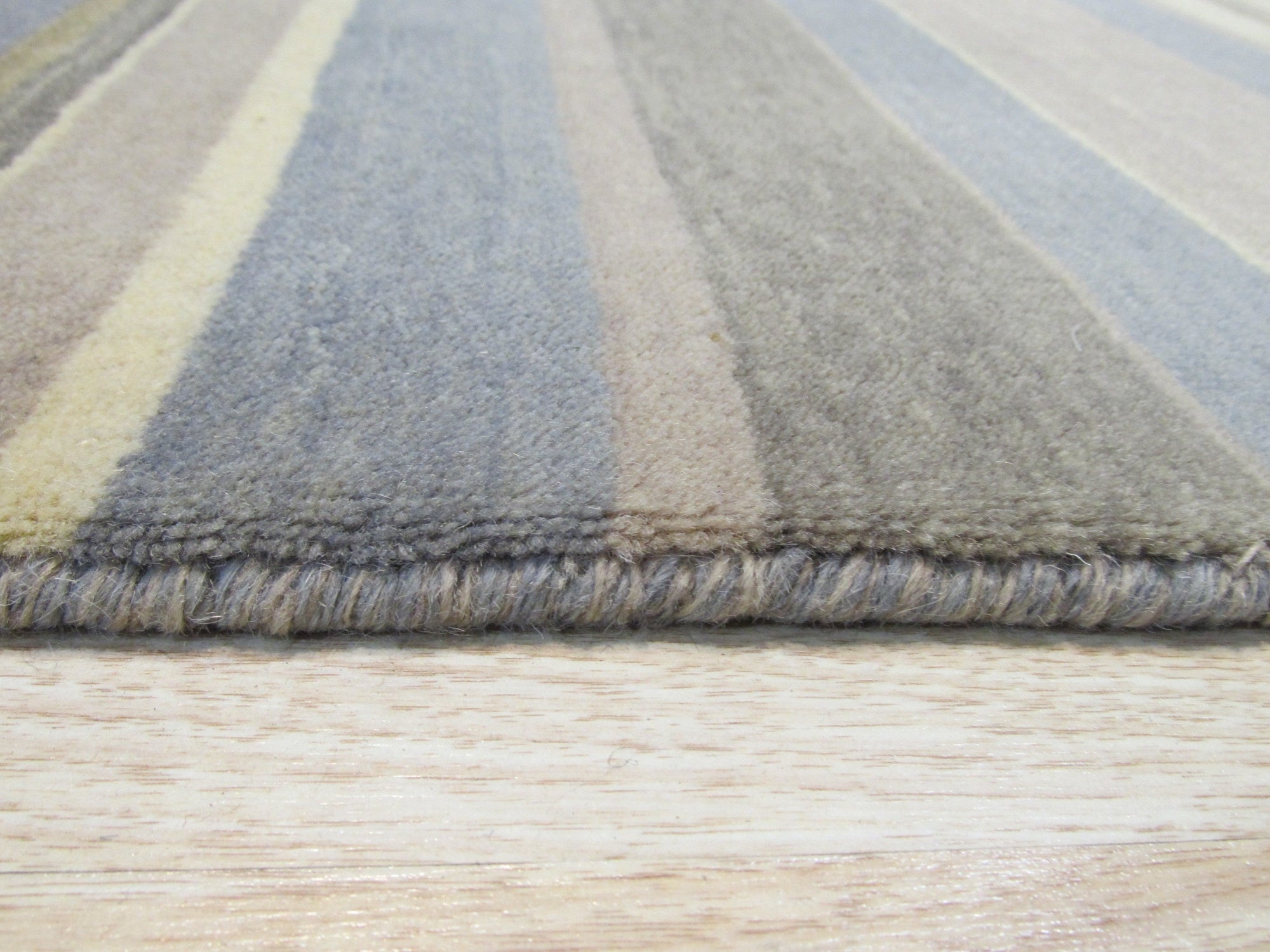 Ella Rustic Brown Handmade Wool Rug, showcasing its warm, earthy tones and subtly textured wool pile, lies partially visible beneath a modern sofa with light wood legs, suggesting a cozy, inviting living space.