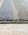Ella Rustic Brown Handmade Wool Rug, showcasing its warm, earthy tones and subtly textured wool pile, lies partially visible beneath a modern sofa with light wood legs, suggesting a cozy, inviting living space.