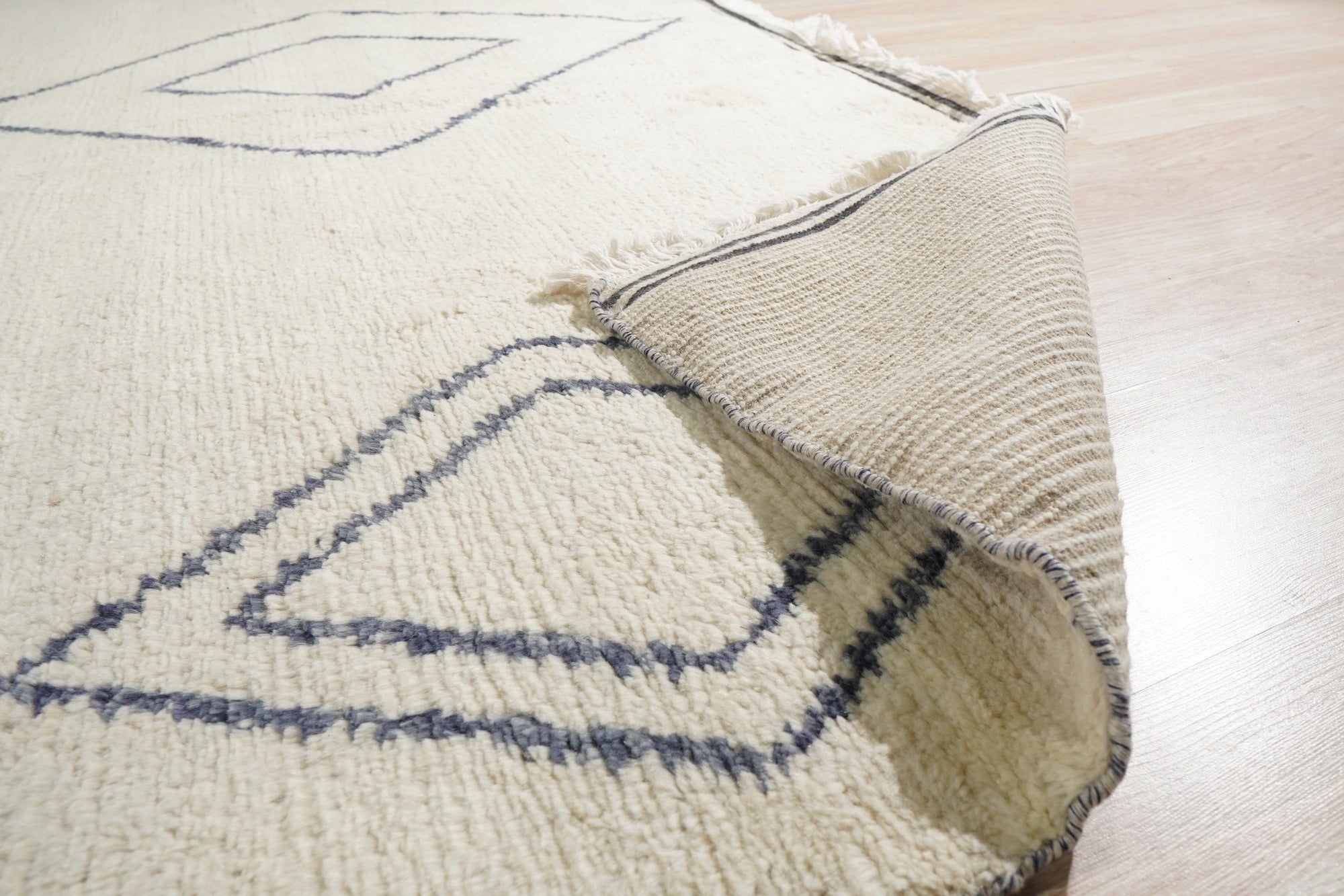 Selene Moroccan Ivory Hand Knotted Wool Rug gracing a light, airy living room. Plush pile invites bare feet, showcasing its intricate geometric pattern in subtle ivory tones, a hand-knotted testament to artisan craftsmanship.