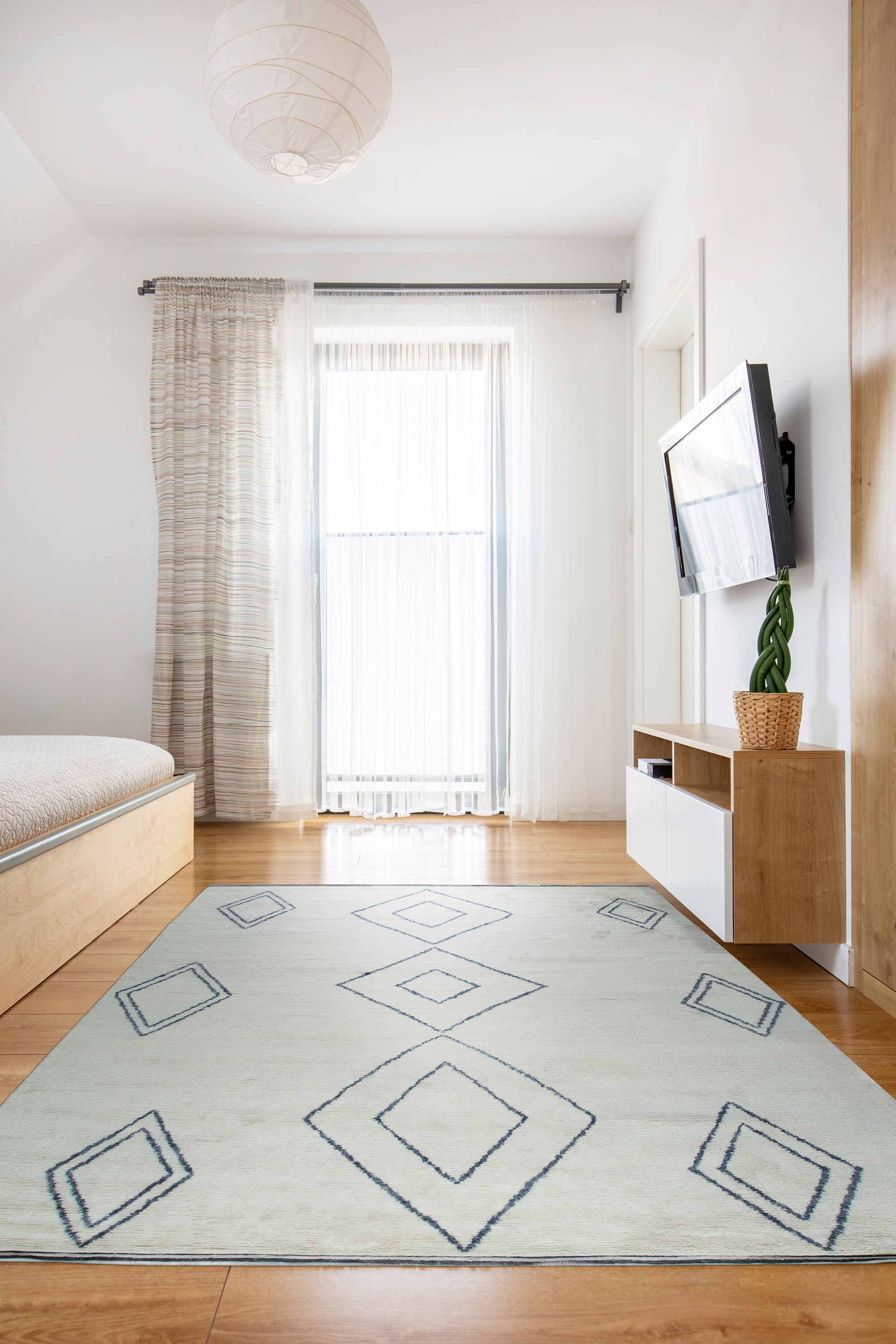 Selene Moroccan Ivory Hand Knotted Wool Rug, with a textured, neutral palette, lies softly on a light wood floor, its subtle geometric pattern complementing the minimalist room bathed in natural light.