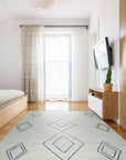 Selene Moroccan Ivory Hand Knotted Wool Rug, with a textured, neutral palette, lies softly on a light wood floor, its subtle geometric pattern complementing the minimalist room bathed in natural light.