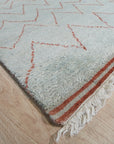 Isla Moroccan Blue Hand Knotted Wool Rug, with a geometric design in shades of blue and off-white, anchors a light-filled living room with hardwood floors and a cozy seating arrangement.