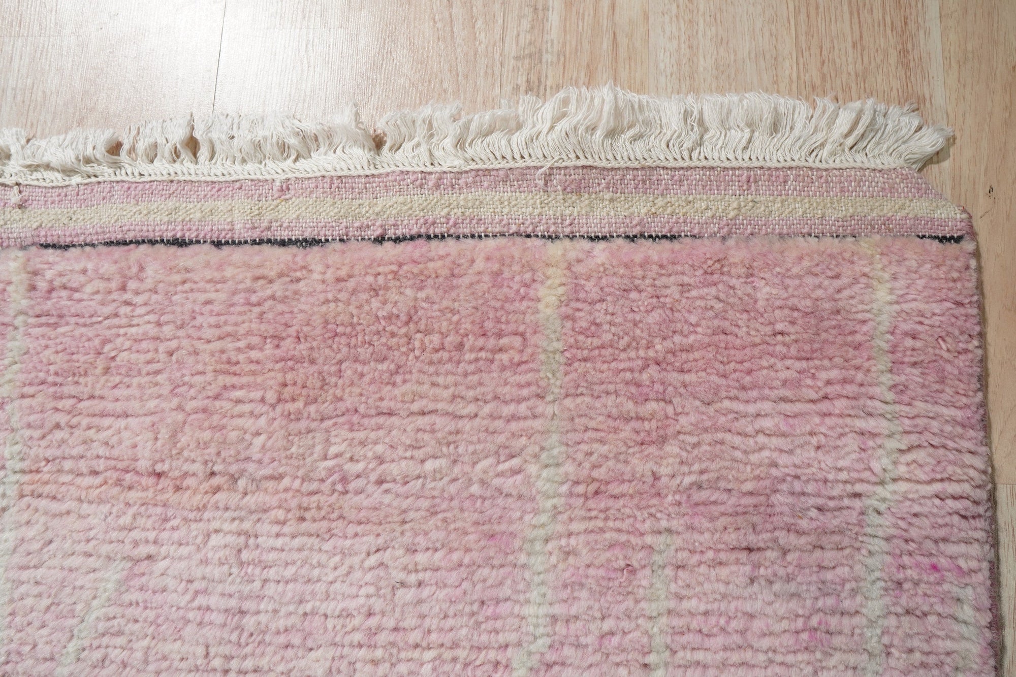 Rhea Moroccan Pink Hand Knotted Wool Rug, presented in a bright, airy room setting with natural light highlighting its textured, hand-knotted construction. The rug's pink hues and intricate Moroccan-inspired design bring warmth and character to the space.