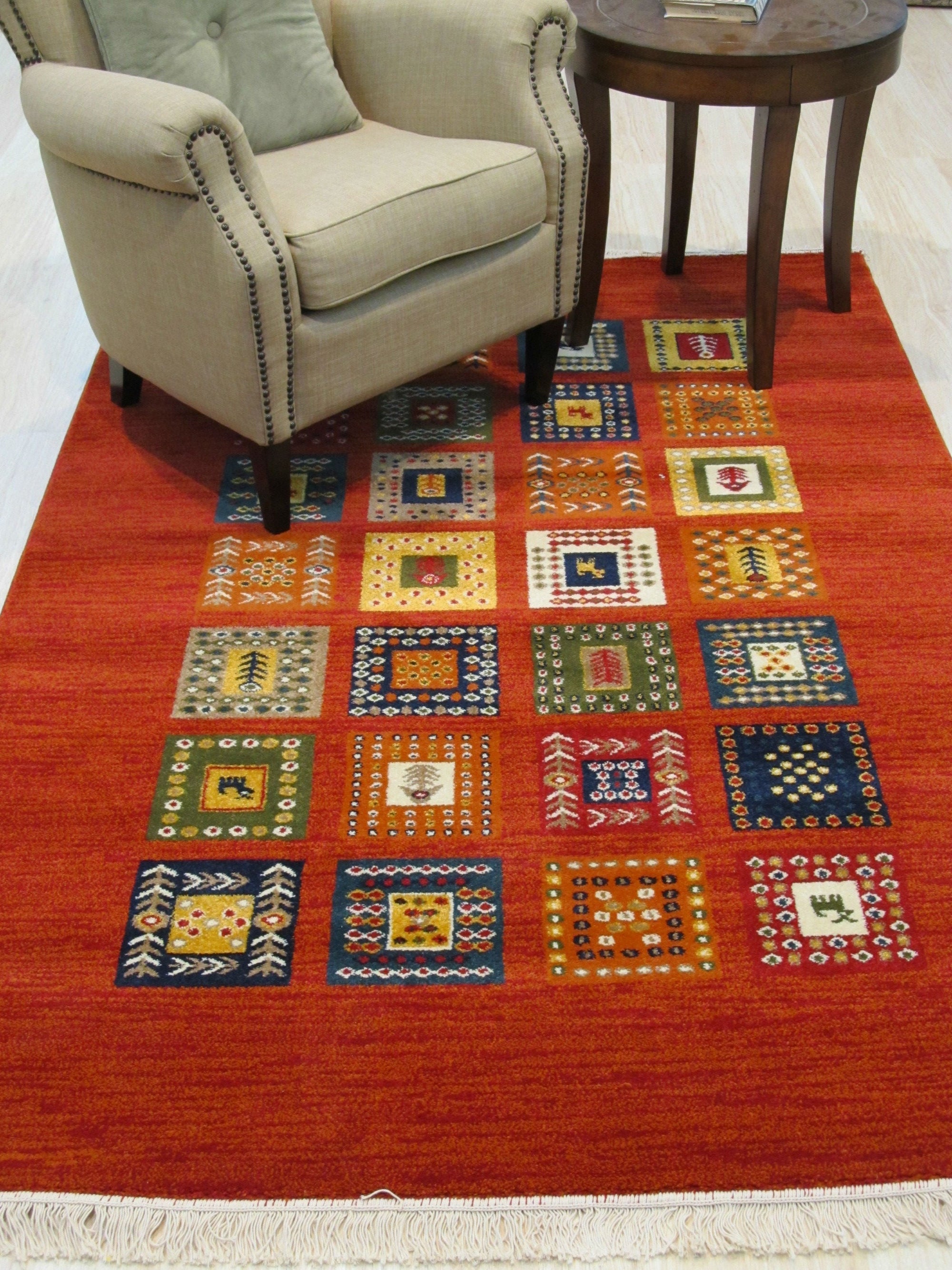 Classic Artisan Red Machine Made Wool Rug, featuring intricate patterns in shades of red, cream, and navy, layered upon a dark hardwood floor. The rug's machine-made wool construction is visible in its dense pile and precise design.