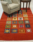 Classic Artisan Red Machine Made Wool Rug, featuring intricate patterns in shades of red, cream, and navy, layered upon a dark hardwood floor. The rug's machine-made wool construction is visible in its dense pile and precise design.