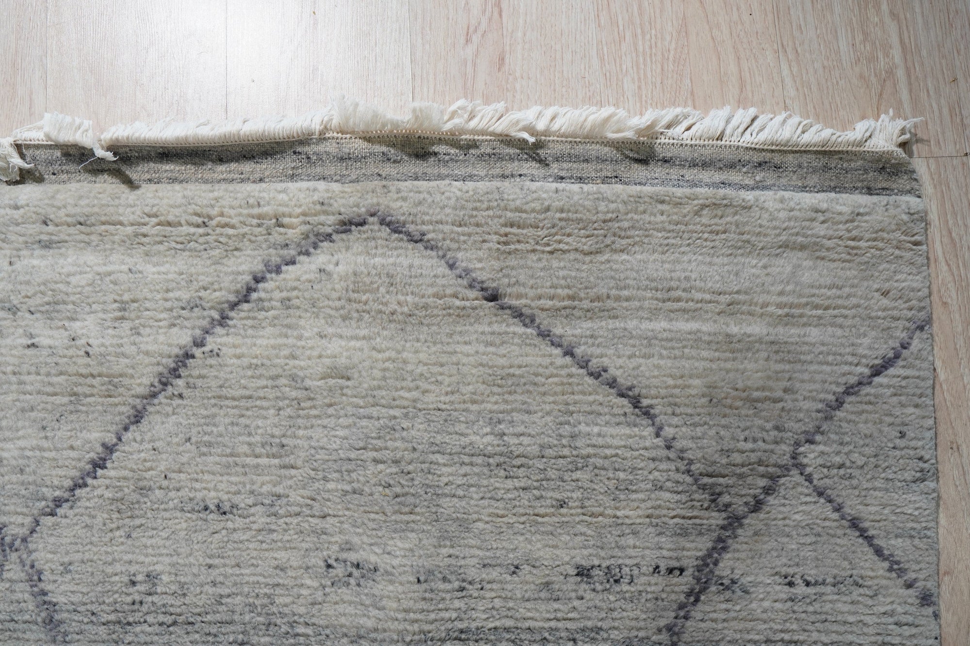 Penelope Diamond Silver Hand Knotted Wool Rug, a luxurious hand-knotted wool rug in silvery tones, gracing a light wood floor with its diamond pattern.