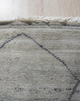 Penelope Diamond Silver Hand Knotted Wool Rug, a luxurious hand-knotted wool rug in silvery tones, gracing a light wood floor with its diamond pattern.