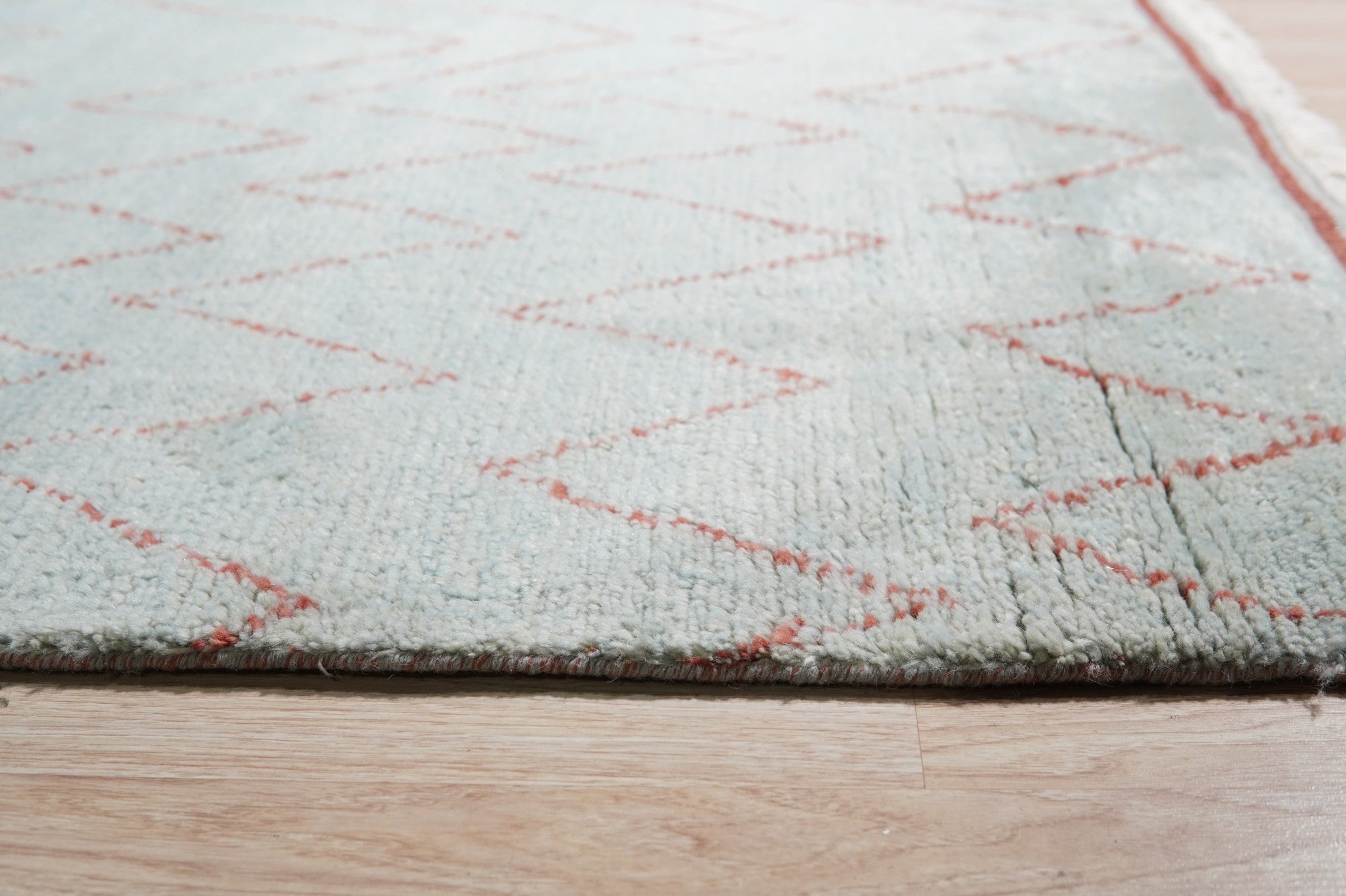 Isla Moroccan Light Blue Hand Knotted Wool Rug, bathed in soft light, features a subtle, geometric pattern in light blue and ivory wool, lending a serene, textured warmth to a contemporary living space.