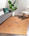 Fiona Penelope Coral Flatweave Rug, a vibrant flatweave in warm coral hues, rests on a polished wood floor, its subtle geometric pattern adding texture and inviting comfort to the sunlit room.